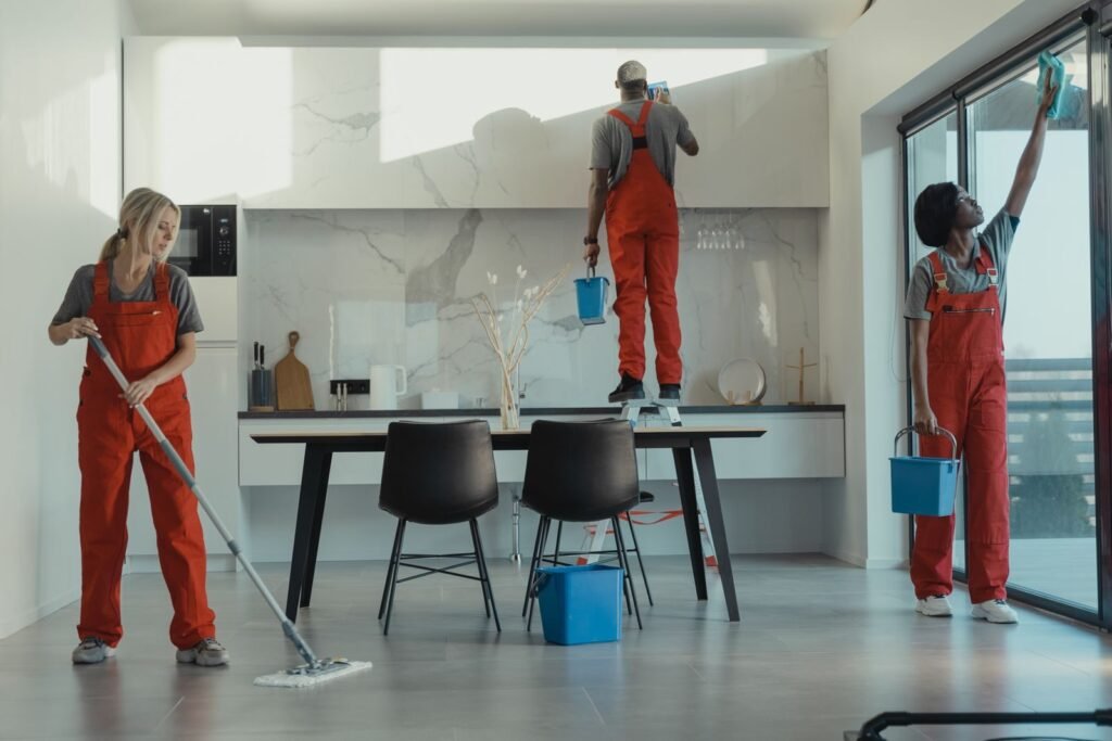 Group of cleaners in red uniforms mopping and wiping glass while villa cleaning services